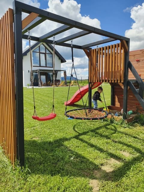 Modern playground with red swings and round trampoline under black metal frame structure with wooden panels and slide attachment