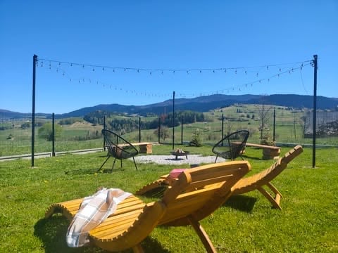 Yellow wooden lounge chairs in a grassy field with mountains in background and string lights overhead