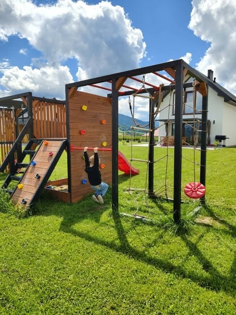 Child playing on wooden climbing structure with metal monkey bars in sunny backyard with mountains in background