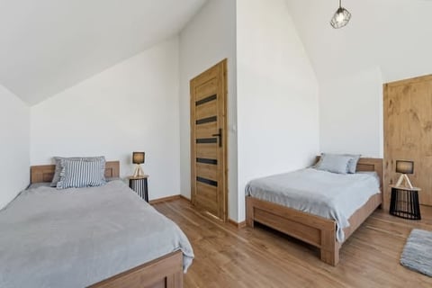 Modern attic bedroom with two wooden beds, white walls, sloped ceiling, wooden doors, and warm wood flooring