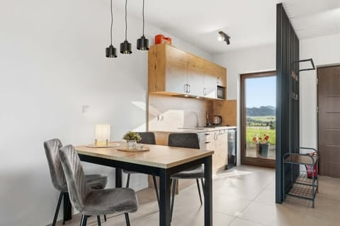 Modern kitchen and dining area with wooden cabinets, black dining table, gray chair, and pendant lights overlooking a countryside view