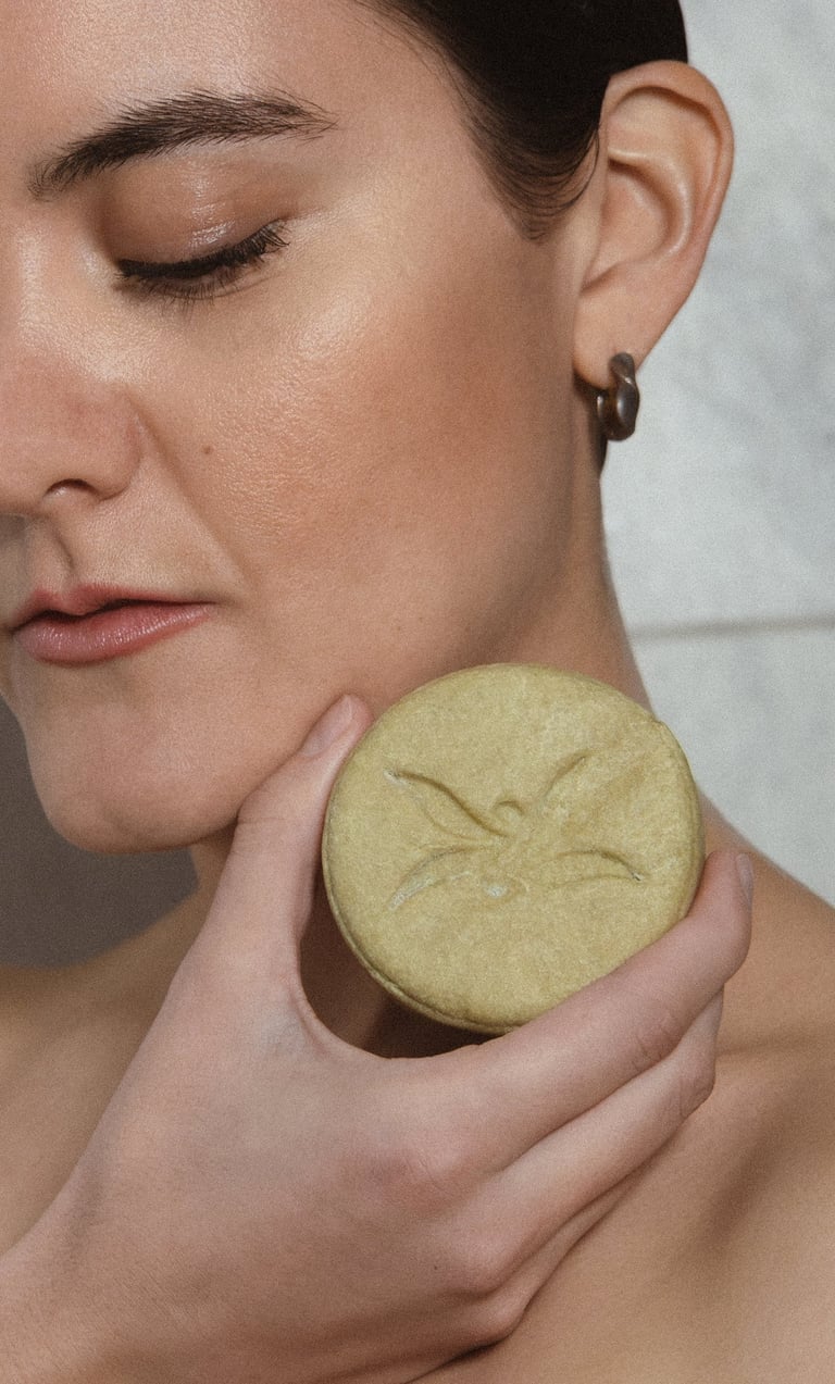 Woman holding a green circular facial soap or sponge against her cheek with eyes closed