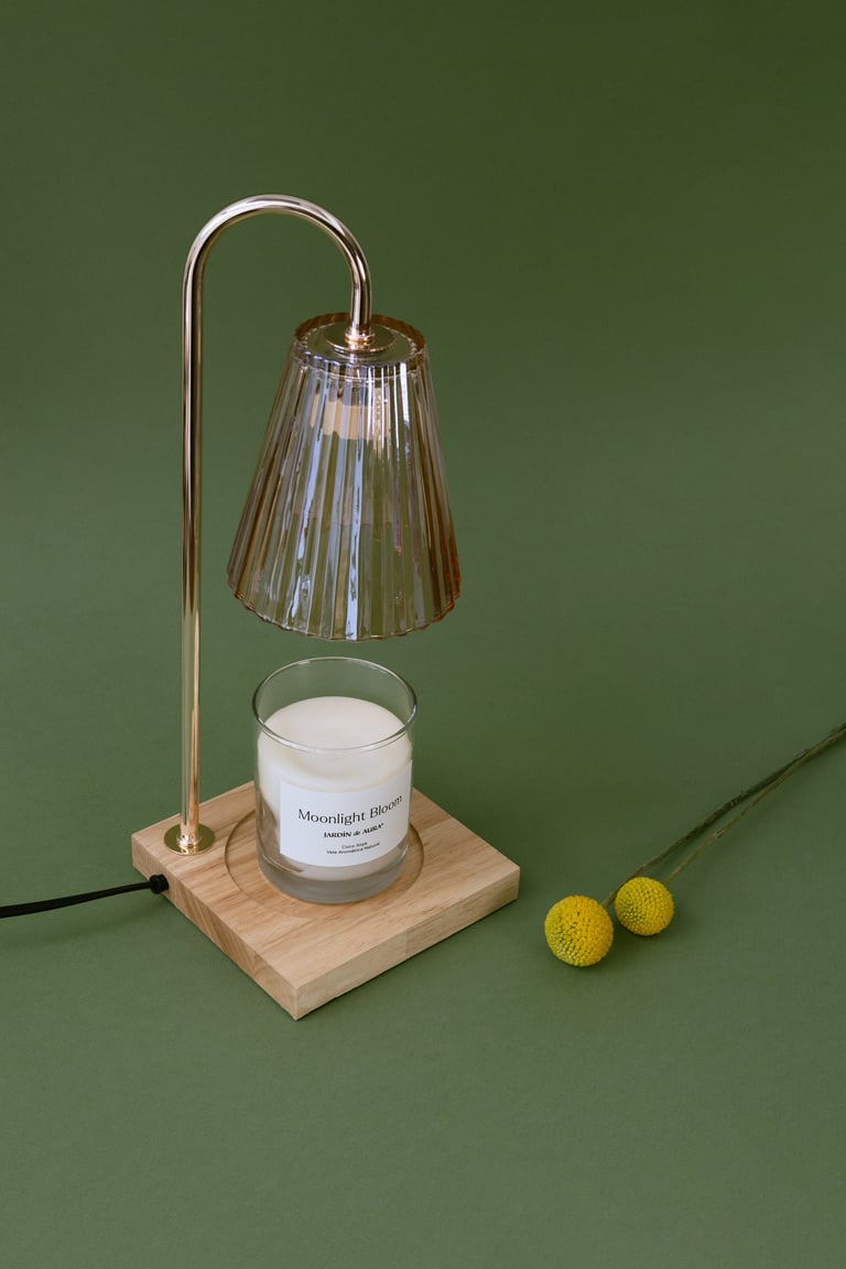 Wooden candle warmer with arched metal frame, ribbed glass shade, and lit candle on green background with two yellow balls