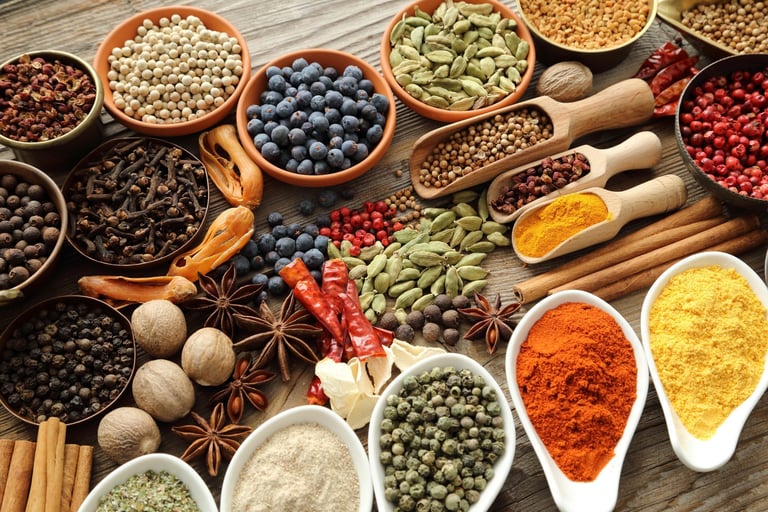 Overhead view of various spices, legumes, and grains in bowls and white dishes, including turmeric, paprika, cinnamon, star anise, and lentils