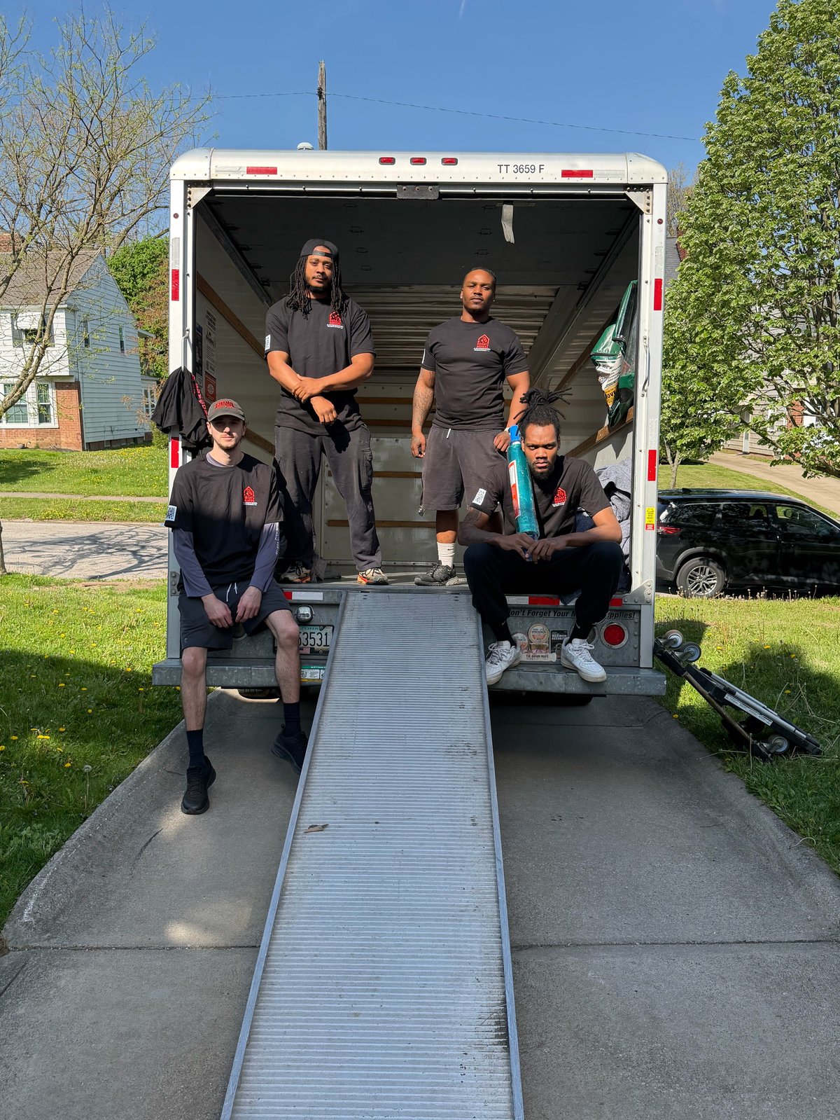 Five people in black uniforms posing in and around the open cargo area of a white moving truck