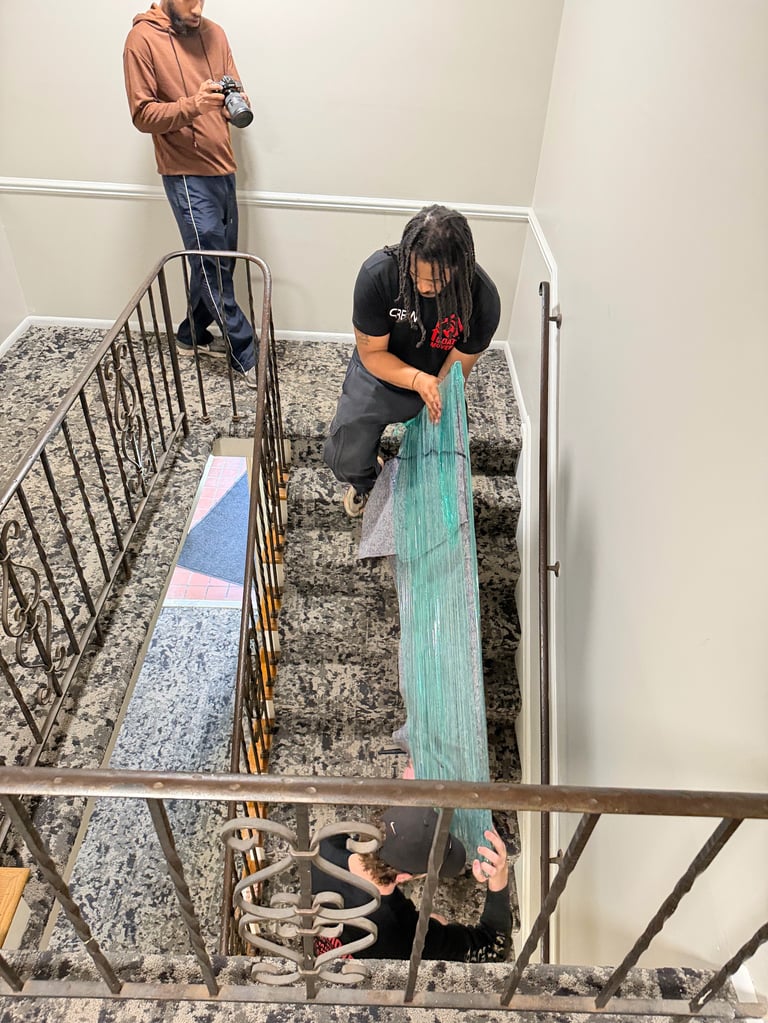 Two people demonstrating flooring samples on a staircase in an indoor space, one crouching and one standing.