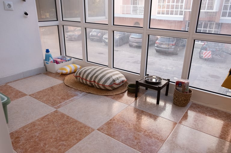 Modern apartment interior with checkered flooring, large windows overlooking a city street, striped cushion seating, and decorative table items