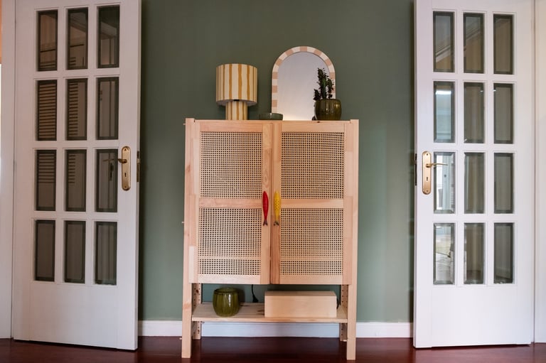 Modern wooden cabinet with rattan doors between two white glass-paned doors against a sage green wall, decorated with a mirror and accessories
