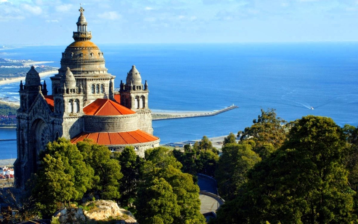 Basilica of the Sacred Heart with golden dome and red roof overlooking coastline and blue sea surrounded by trees