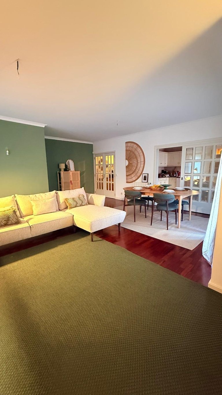 Modern living room with yellow sectional sofa, green accent wall, green carpet, and dining area visible through open doorway
