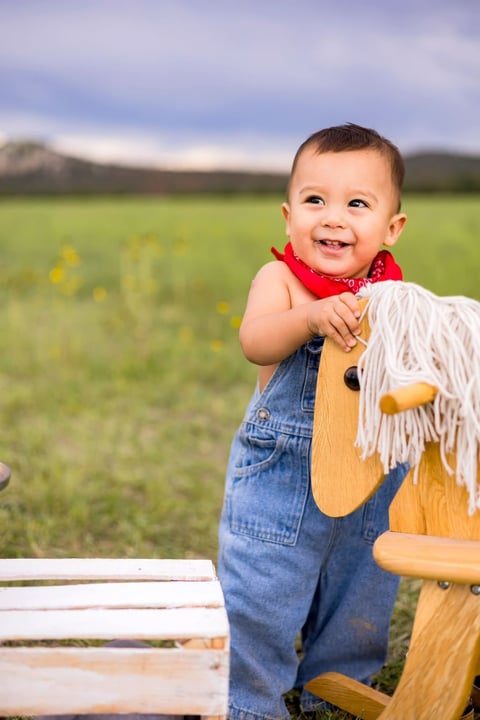 Andrés con overol de mezclilla jugando con un caballito de madera