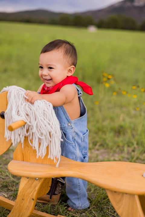 Andrés con caballito de madera en un campo con montañas