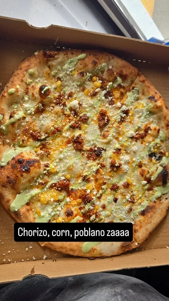 Pizza topped with chorizo, corn, poblano peppers, cheese, and seasonings in a cardboard box