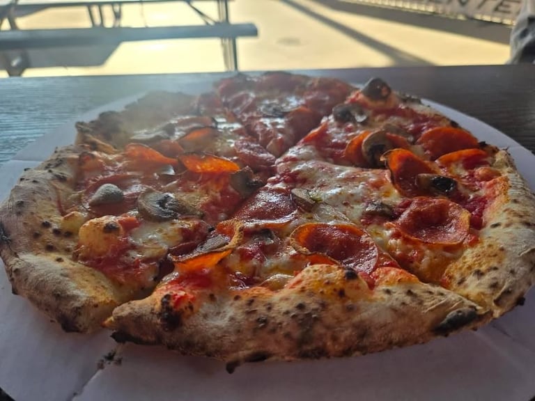 Pepperoni and vegetable pizza on a white plate with waterfront and railing visible in background