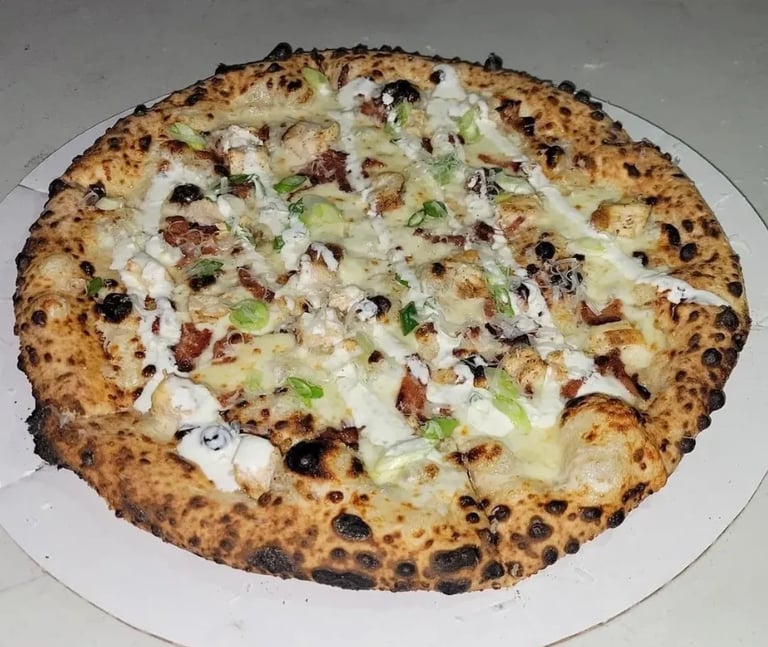 Gee Jay's Chicken Bacon Ranch wood-fired pizza with white sauce, bacon, mushrooms, and herbs on a charred crust, served on a white plate