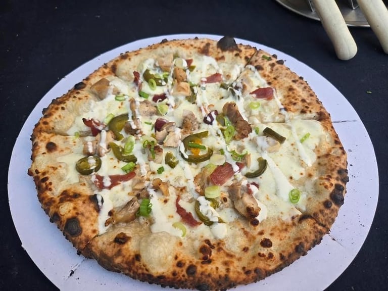 Artisan pizza with white sauce, cheese, bacon, and green peppers on a charred crust