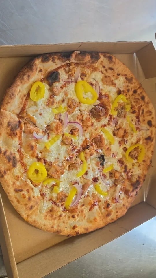 A pizza in a cardboard box topped with cheese, meat, yellow peppers, and onions