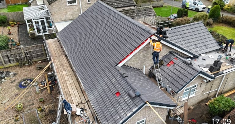 Aerial view of roofers installing dark metal roofing tiles on residential house with neighborhood houses visible in background