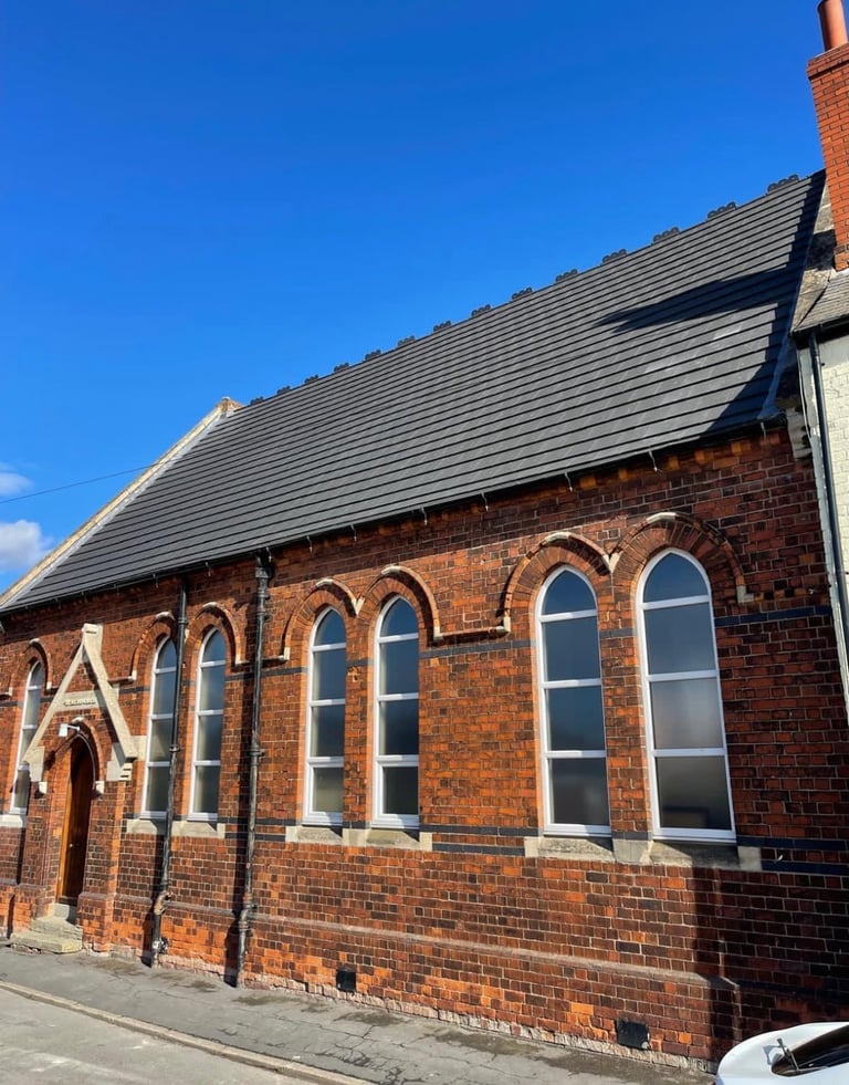 Red brick church building with slate roof and arched windows under clear blue sky