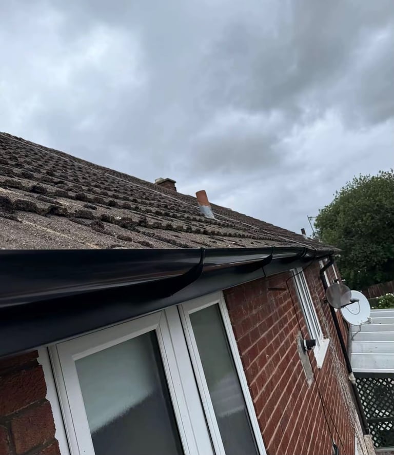 Brick house roof with aged shingles, white-framed windows, black gutters, and overcast sky