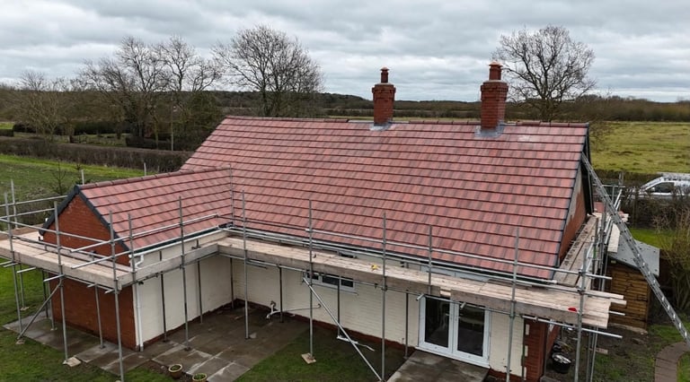 Residential house with new red roof installation and scaffolding, set in rural countryside landscape with bare trees