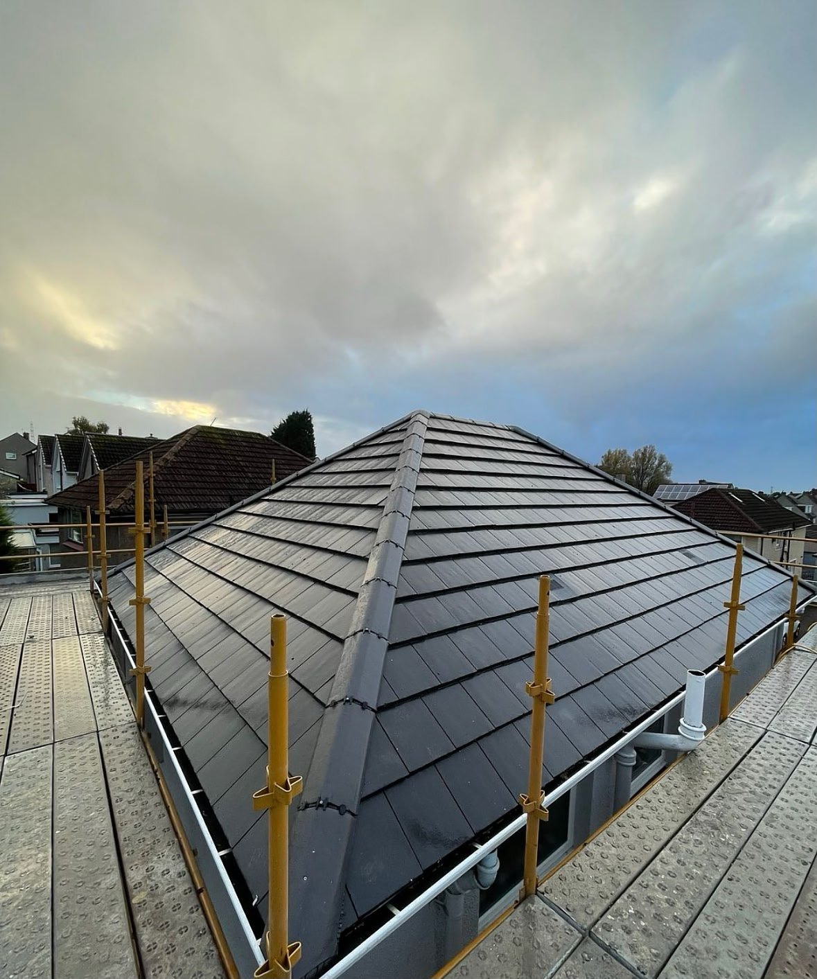 New black metal roof on residential house under construction with yellow safety railings and cloudy sky