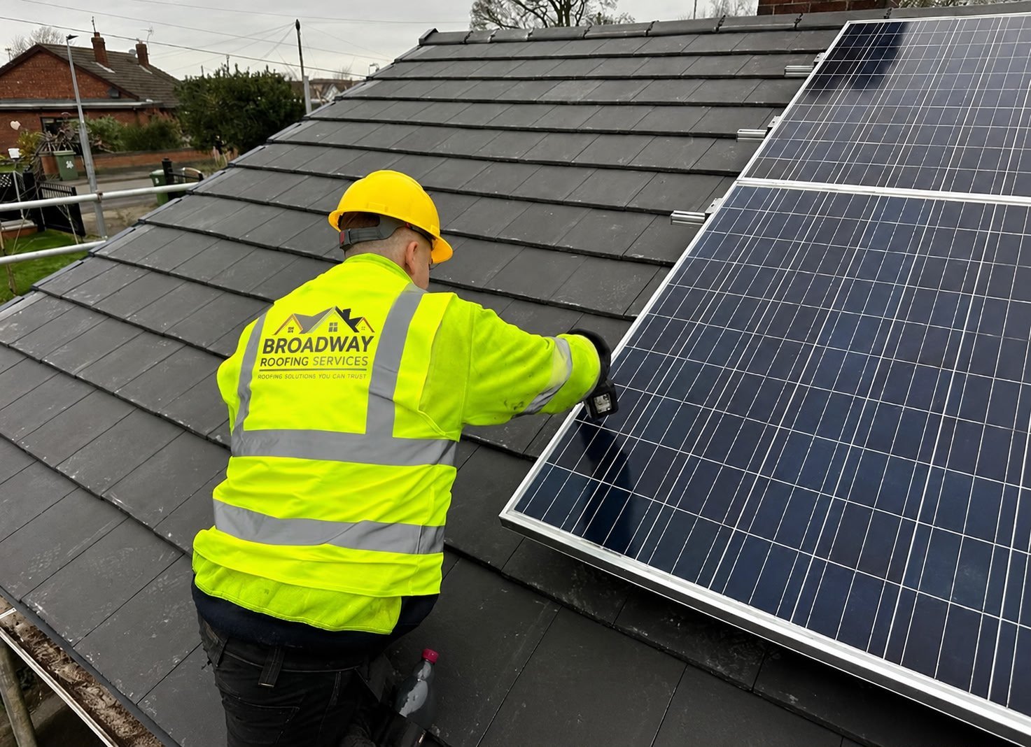 Construction worker in high-visibility gear installing solar panels on a residential roof