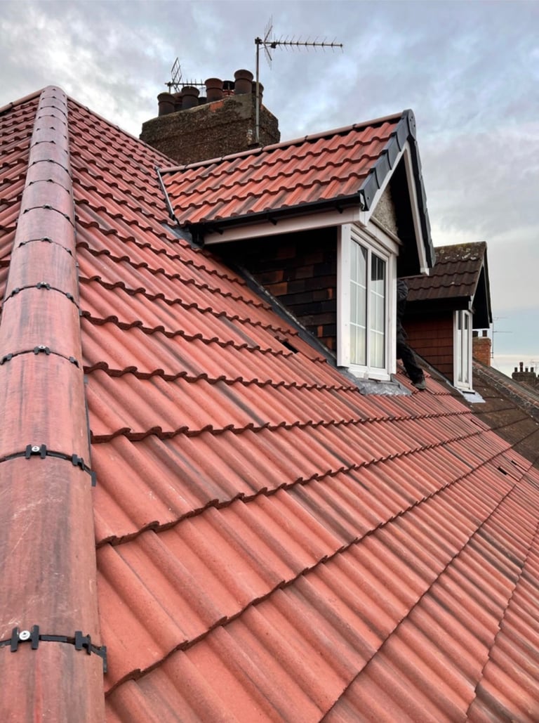 Red clay tile roof with dormer window, brick chimney, and television antenna visible against cloudy sky