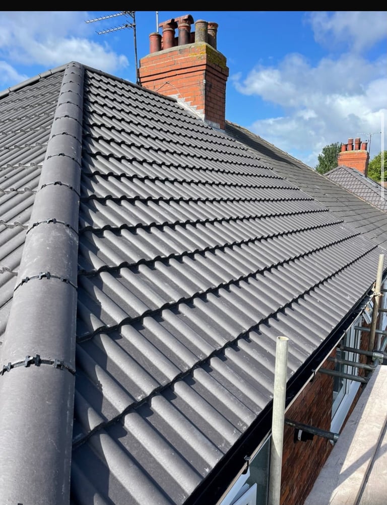 Modern gray slate roof with red brick chimneys against blue sky with clouds
