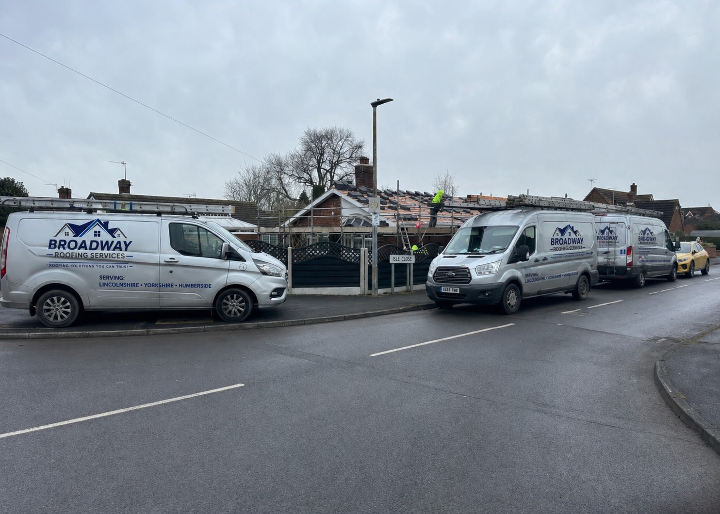 Multiple white service vans parked on a street outside a brick building on an overcast day