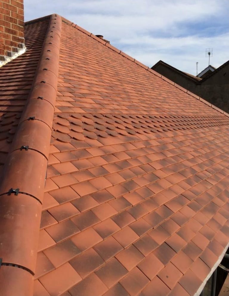 Red clay tile roof with downspout and brick chimney against cloudy sky