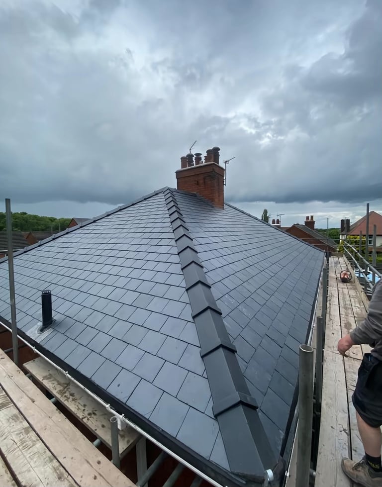 Newly installed gray slate roof on house with red brick chimney against cloudy sky, taken from roofline view