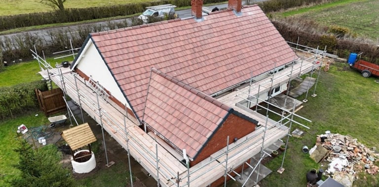 Aerial view of a residential house under renovation with new red tile roof and metal scaffolding during construction