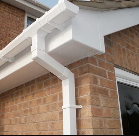White PVC guttering and downpipe installed on red brick house exterior wall near window.
