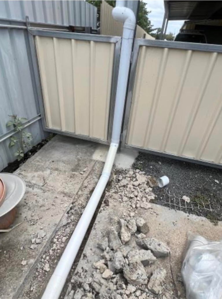 Two metal-frame corrugated panels with white PVC pipe running between them on gravelly ground
