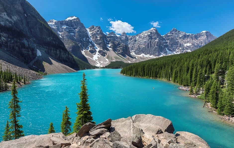 Turquoise alpine lake surrounded by pine forests and snow-capped mountains under clear blue sky
