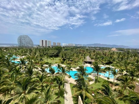 Aerial view of resort with turquoise pools, palm trees, and modern high-rise buildings against blue sky