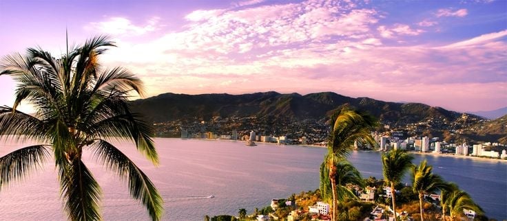 Atardecer tropical en la bahía de Acapulco con palmeras y montañas