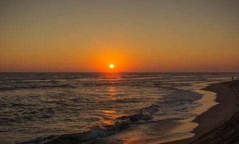 Sunset over the ocean with golden sun reflecting on the water and waves rolling onto a sandy beach at dusk