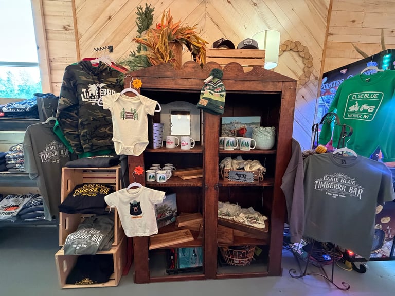 Wooden display shelf with merchandise including folded t-shirts, apparel, and decorative items in a retail shop setting