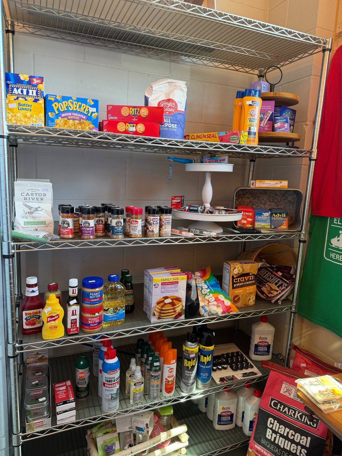 Wire shelving stocked with snacks, popcorn, sauces, spices, oils, charcoal, and pantry essentials