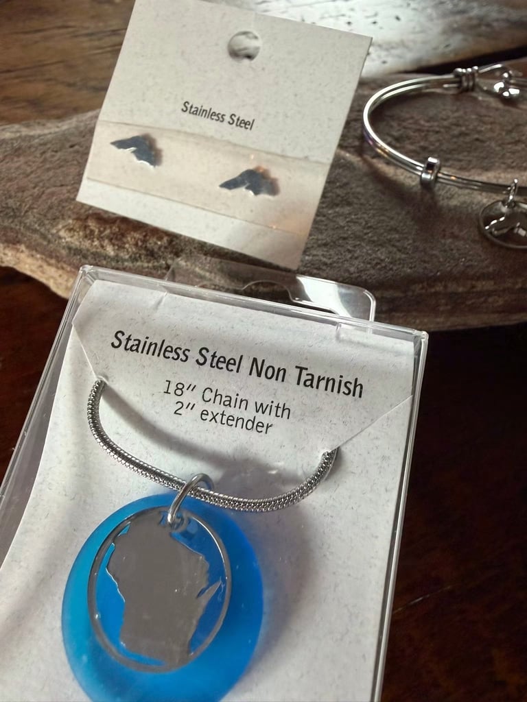 Stainless steel jewelry collection including bird stud earrings, bangle bracelet, and blue pendant necklace on wooden surface