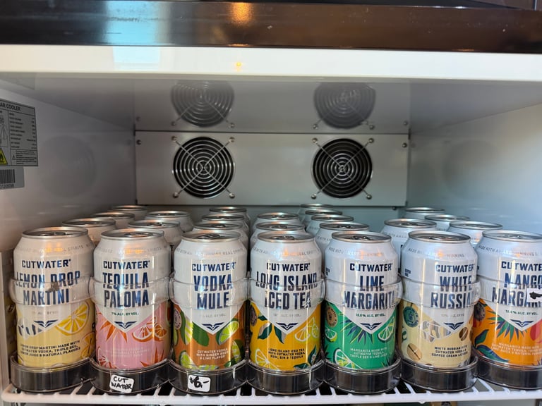 Refrigerator shelf stocked with Cutwater canned cocktails in seven flavors: Lemon Drop Martini, Tequila Paloma, Vodka Mule, Long Island Iced Tea, Lime Margarita, White Russian, and Mango Margarita