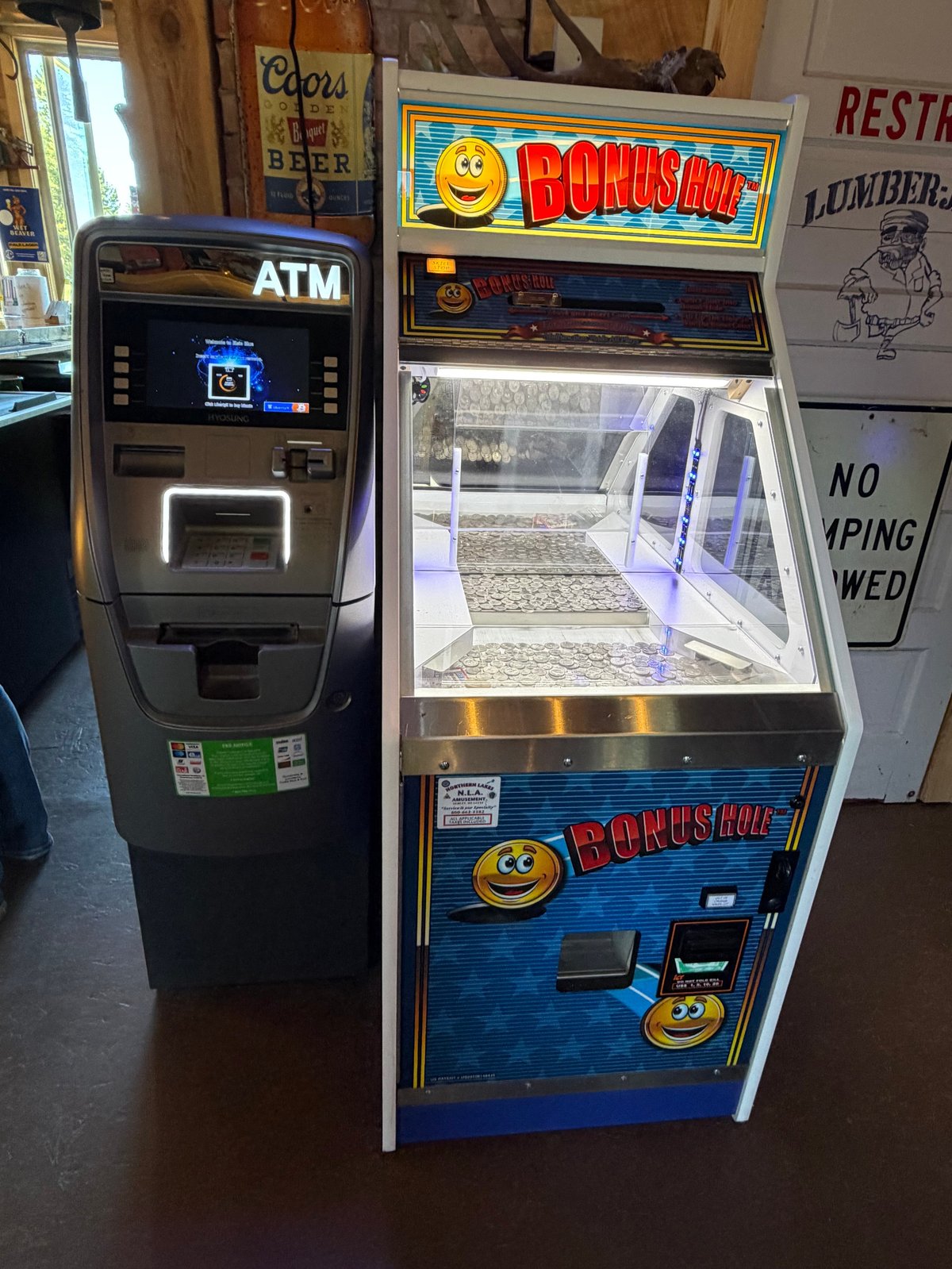 Hyosung ATM next to a vintage Bonus Hole coin pusher arcade game with smiley face graphics in the bar entryway
