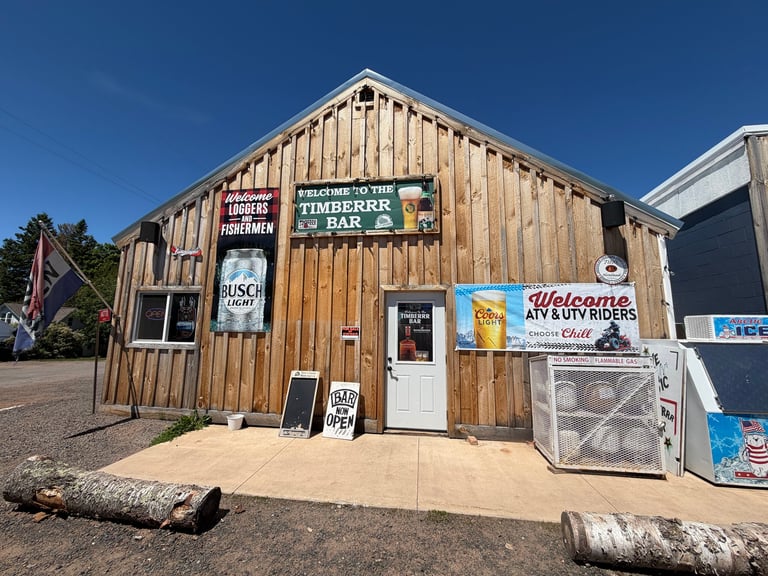 Timberrr Bar front with welcome sign, Busch Light and Coors Light beer banners, and ATV/motorcycle/snowmobile welcome banner