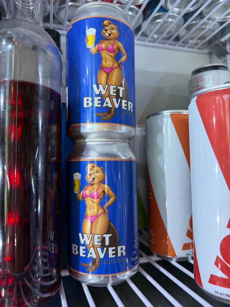 Two blue Wet Beaver Pale Lager beer cans stacked on a cooler shelf with other beverages