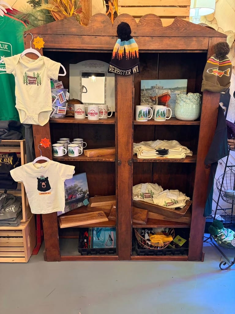 Wooden display shelf unit showing merchandise including infant onesies, mugs, photos, and textiles arranged on multiple shelves