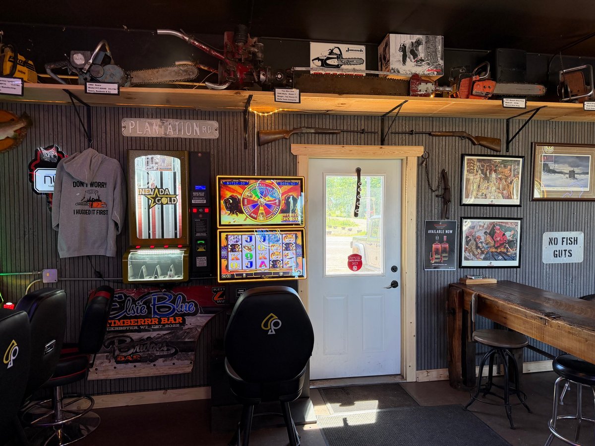 Corrugated metal wall displaying antique chainsaws on high shelves above a gold mine arcade game and a Nevada Gold game at the bar entrance