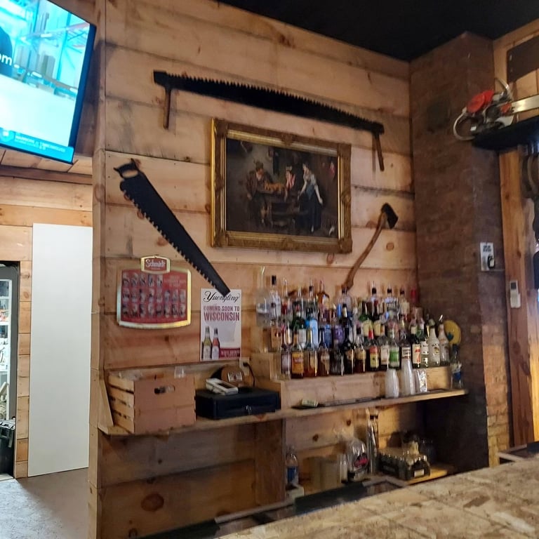 Rustic wooden wall display with vintage tools, framed artwork, and collection of liquor bottles in a casual bar or tavern setting