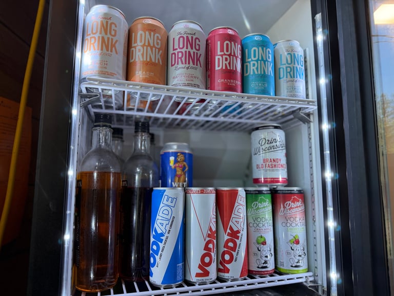 Refrigerator shelf displaying Wet Beaver beer, Vodkaade vodka cocktails in Diet and regular, and Drink Wisconsin Brandy Old Fashioned and Vodka Cocktails